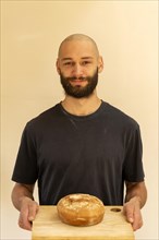 Head and shoulder portrait Caucasian white young man shaven head and beard holding fresh loaf of