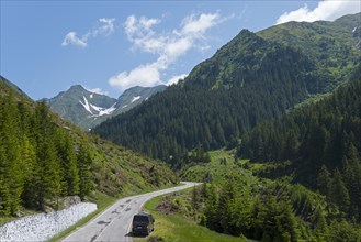 Road leading through a picturesque mountain landscape with lush greenery and clear blue skies,