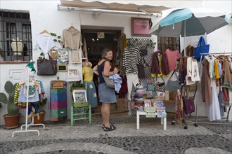 Woman tourist outside souvenir shop, Frigiliana, Axarquia, Andalusia, Spain display of clothes and