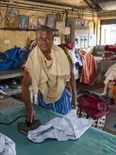 A man irons shirts with an antique iron at Dhobi Khana Public Laundry, Fort Kochi, Cochin, Kerala,