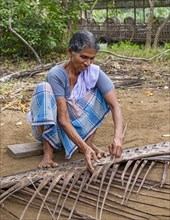 A village woman demonstrates the traditional craft of making mats from coconut leaves using her