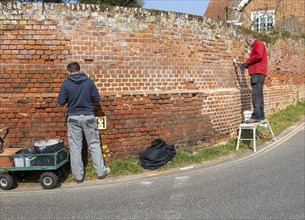 Two men repointing old red brick wall, Orford, Suffolk, England, UK