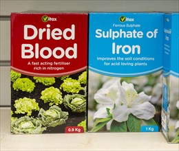 Cardboard boxes of Vitax Dried Blood and Sulphate of Iron on shelf display in garden centre, UK
