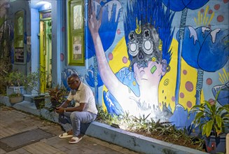 Man sits on a curb in front of illuminated street art in the streets of Fort Kochi, Cochin, Kerala,