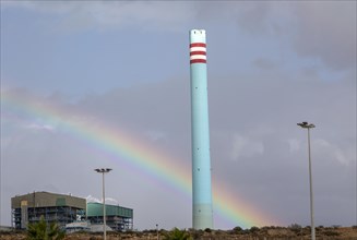 Rainbow in stormy sky behind tall blue industrial cement factory chimney, Carboneras, Almeria,