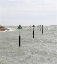 Green triangular warning markers on posts in shallow water at River Orwell river mouth, Landguard