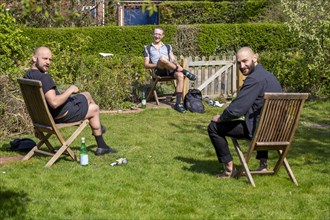 Three men having a socially distanced chat in a garden, UK during Covid-19 Coronavirus lockdown