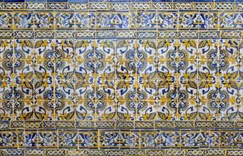 Antique floral decorated Azulejo ceramic tiles in yellow, white and blue colours on wall inside a
