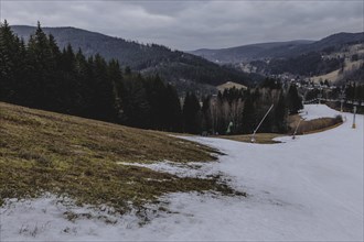 A melting ski slope next to a meadow, taken on a ski slope in the Jizera Mountains ski area near