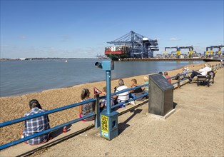 People on beach at viewing area watching shipping in Port of Felixstowe, Suffolk, England, UK