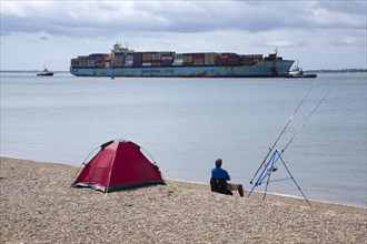 Fisherman watches arrival of Maersk Utah container ship at Port of Felixstowe, Suffolk, England, UK