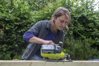 Young woman using electric power sawing tool without safety googles or protective clothing, model
