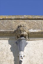 Gargoyle grotesque face drainpipe on wall medieval church of Saint John, Inglesham, Wiltshire,