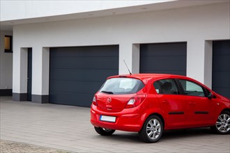 An Opel Corsa is parked in front of one of several garages with black sectional doors