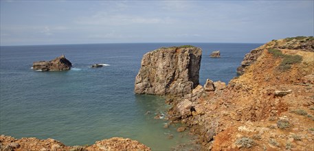 Coastal stacks and stumps orange coloured crumbling cliffs rise from Atlantic Ocean at Cabo de Sao