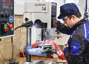 A trainee mechatronics technician works with a bench drill on a workpiece in a Deutsche Bahn