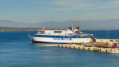 Ferry in the harbour loaded with trucks, surrounded by sea and mountains under a blue sky, Gythio,