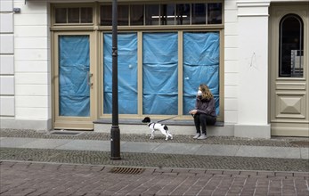 A woman sits with her dog in front of a closed shop. Customers who want to buy in retail stores in