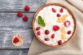 Rice flakes porridge with milk and strawberry in wooden bowl on gray wooden background and linen