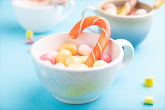 Heap of multicolored caramel candies in cups on blue pastel background. close up, side view,