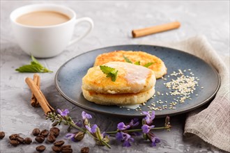 Cheese pancakes on a blue ceramic plate and a cup of coffee on a gray concrete background. side