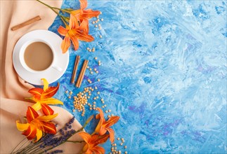 Orange day-lily and lavender flowers and a cup of coffee on a blue concrete background, with orange