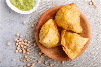 Traditional indian food samosa in wooden plate with mint chutney on a gray concrete background. top