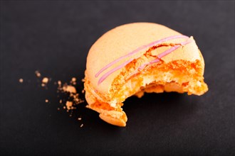 Bitten orange macaron or macaroon cake on black background. side view, close up, macro, selective