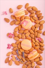 Orange macarons or macaroons cakes with almond nuts on pastel pink background. top view, flat lay,
