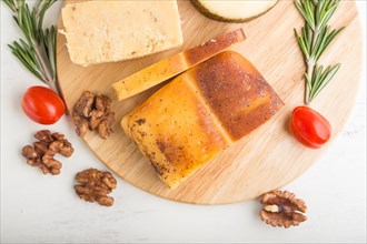 Smoked cheese and various types of cheese with rosemary and tomatoes on wooden board on a white