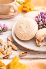 Meringues cakes with cup of coffee on a white wooden background and orange linen textile. Side