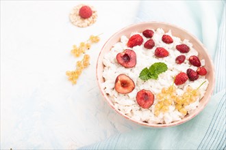 Rice flakes porridge with milk and strawberry in ceramic bowl on white concrete background and blue