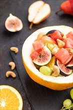 Vegetarian fruit salad of watermelon, grapes, figs, pear, orange, cashew on slate board on a black