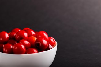 Fresh red sweet cherry in white bowl on black background. side view, copy space, close up