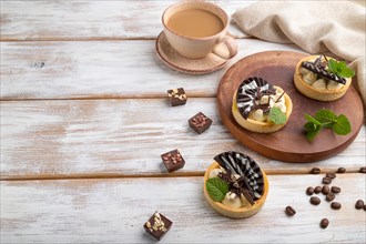 Sweet tartlets with chocolate and cheese cream with cup of coffee on a white wooden background and