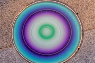 Closeup round glass of blue, green and purple inlaid in concrete sidewalk in public park in South