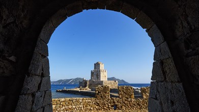 View from an arch onto an old stone watchtower spire in front of a picturesque sea panorama,