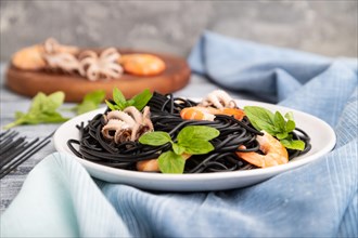 Black cuttlefish ink pasta with shrimps or prawns and small octopuses on gray wooden background and
