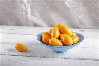 Kumquats in a blue plate on a white wooden background, close up