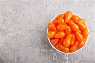 Fresh orange grape tomatoes in white ceramic bowl on gray concrete background. top view, flat lay,