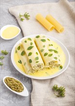 Cannelloni pasta with egg sauce, cream cheese and oregano leaves on a gray concrete background with