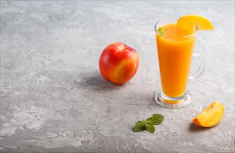 Glass of peach juice on a gray concrete background. Morninig, spring, healthy drink concept. Side