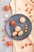 Orange macarons or macaroons cakes on blue ceramic plate on a gray concrete background and orange