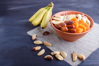 A plate with muesli, banana, dried apricots, dates, Brazil nuts on a black wooden background. close
