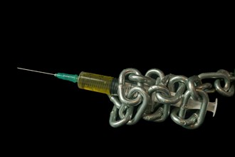 Syringe filled with yellow liquid tied with a chain isolated on black background and copy space,