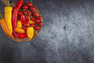 Colourful peppers and tomatoes on a wooden cutting board on a grey background
