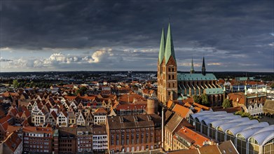 Panorama of a historic city with church towers and roofs under a dramatic evening sky, view from