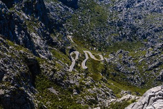 Serpentine road winds through a rocky mountain landscape on a sunny day, Majorca