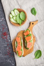 Smoked salmon sandwiches with cucumber and spinach on wooden board on a black concrete background.