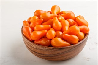 Fresh orange grape tomatoes in wooden bowl on white wooden background. side view, close up